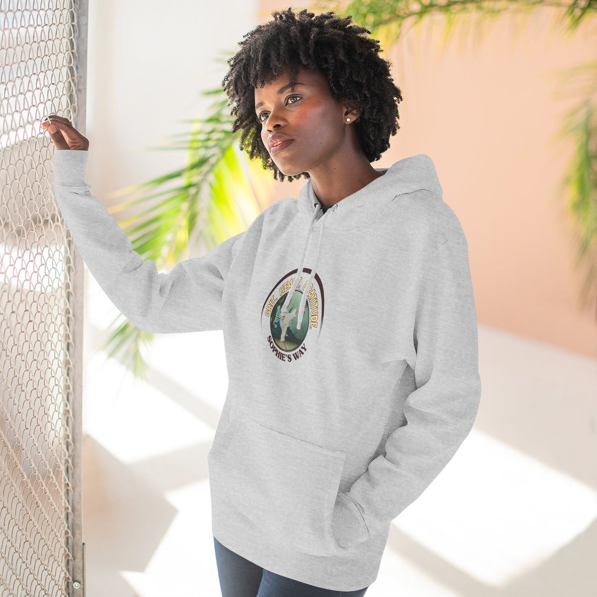 A heather grey pullover hoodie with a circular graphic on the chest that reads 'Grit. Heart. Gratitude. Sophie's Way' around a globe design around a taekwondo tot doing a side kick. The hoodie features a drawstring hood, long sleeves, and a front kangaroo pocket.