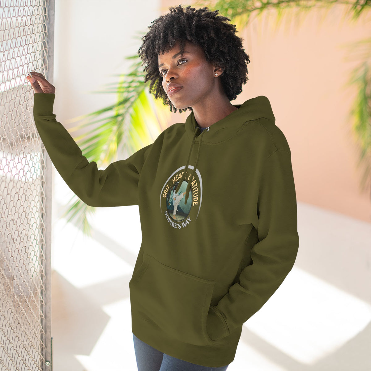 A army green pullover hoodie with a circular graphic on the chest that reads 'Grit. Heart. Gratitude. Sophie's Way' around a globe design. The hoodie features a drawstring hood, long sleeves, and a front kangaroo pocket.