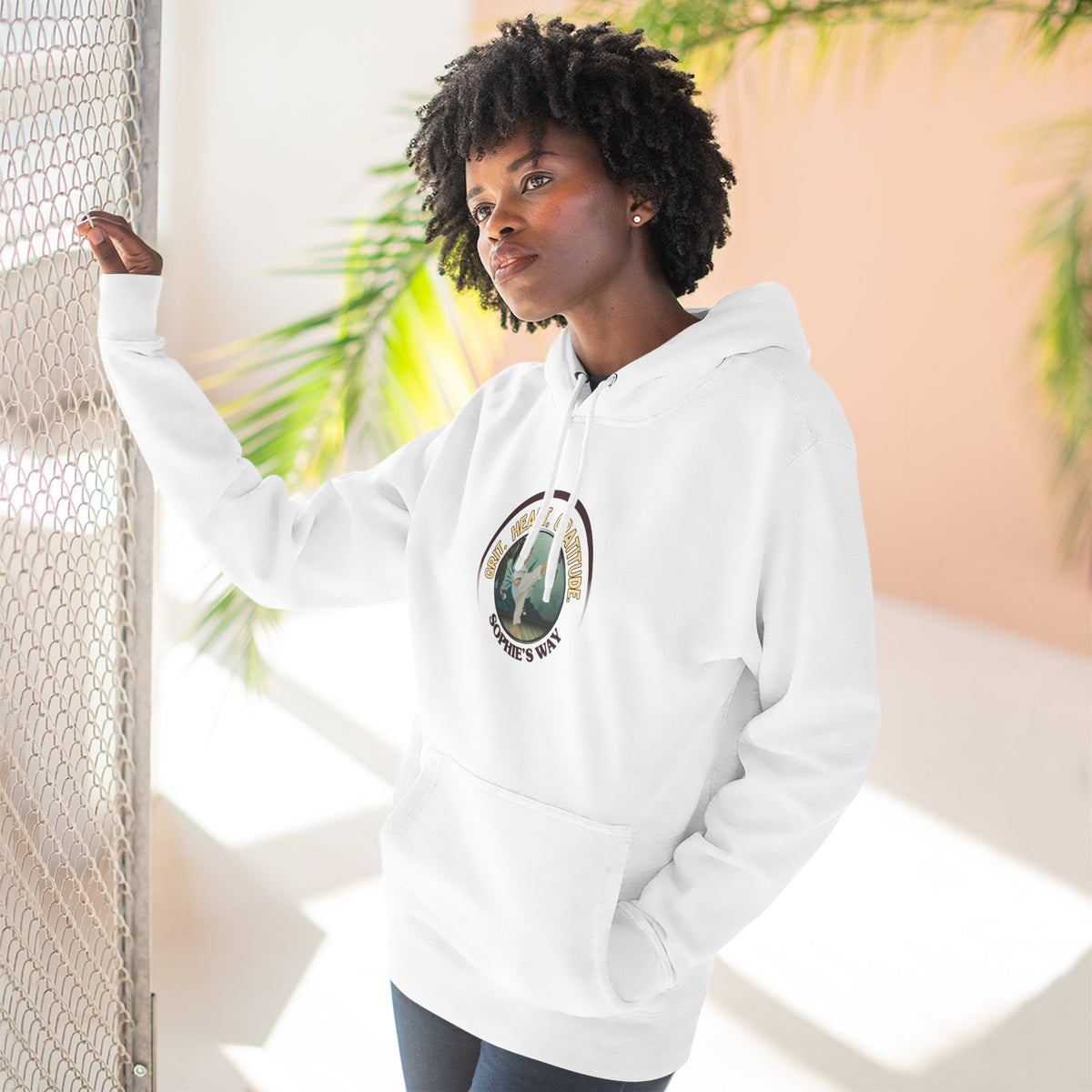 A white pullover hoodie with a circular graphic on the chest that reads 'Grit. Heart. Gratitude. Sophie's Way' around a globe design around a taekwondo tot doing a side kick. The hoodie features a drawstring hood, long sleeves, and a front kangaroo pocket.