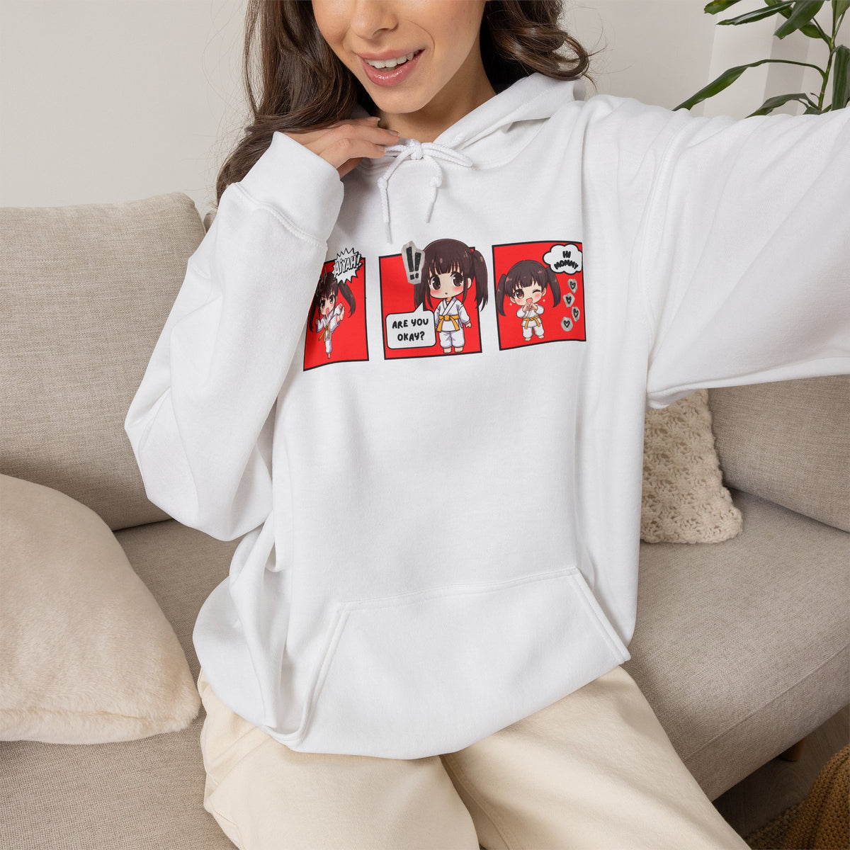 A white pullover hoodie with a red and multicolor anime-style graphic print on the chest of a taekwondo girl saying 'Aiyah!' then 'Are you okay?', and then 'Hi Mommy."