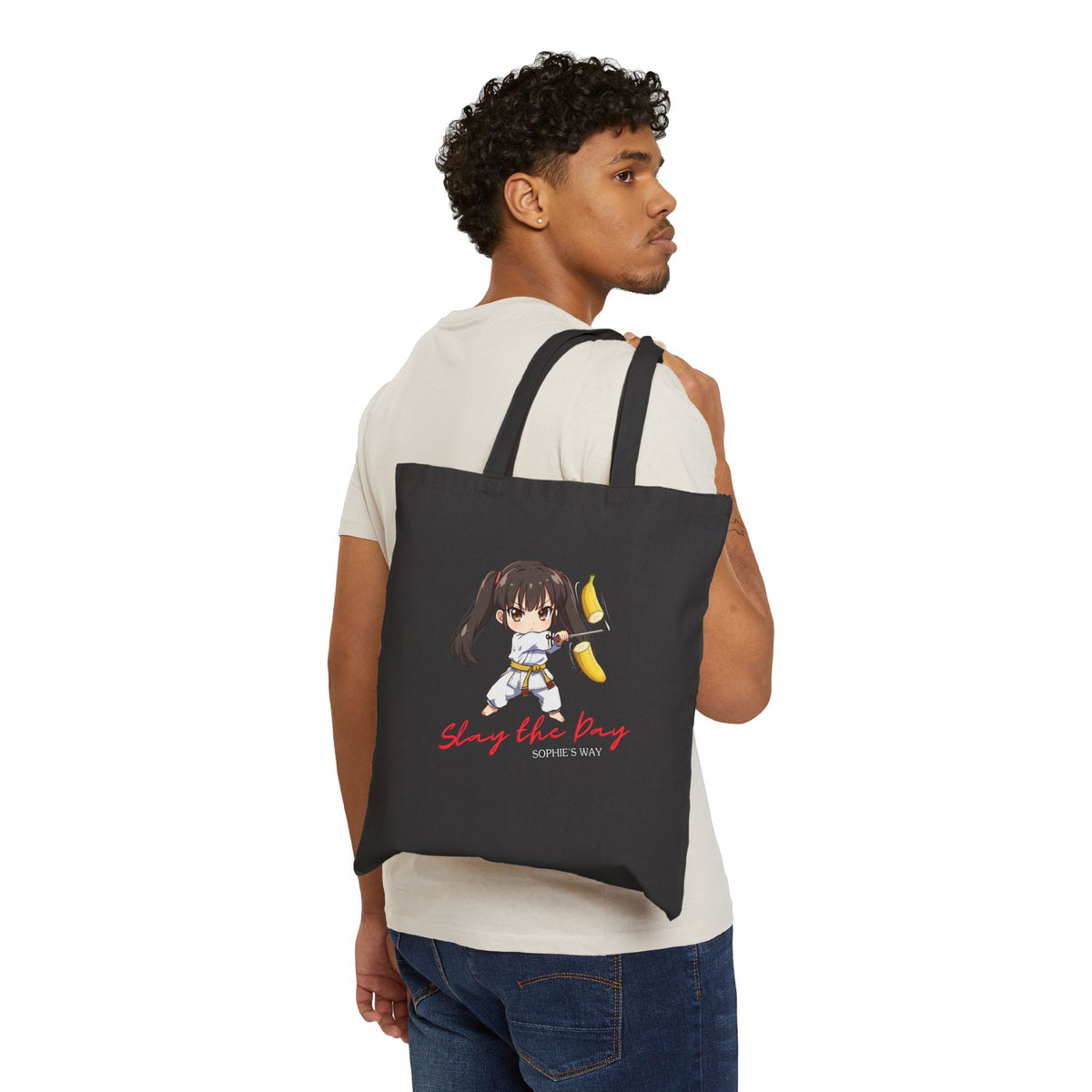Slay the Day cotton canvas tote bag in black, worn on back by man — chibi taekwondo girl slicing a banana with a sword — "Slay the Day, Sophie's Way"