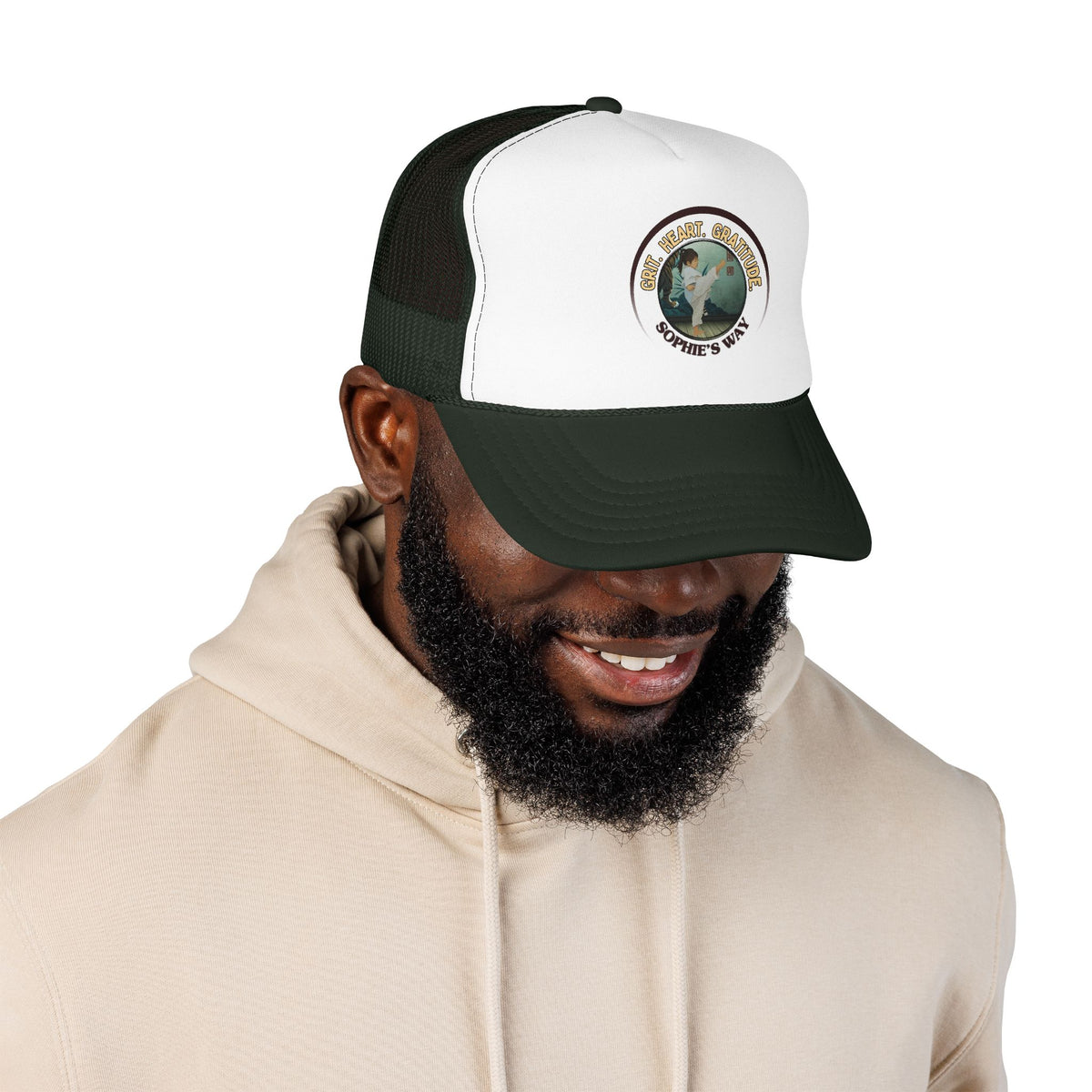 A forest green and white trucker hat with a circular graphic on the front panel. The graphic features a border with the words 'Grit. Heart. Gratitude. Sophie's Way' and a taekwondo tot doing a side kick in the center.