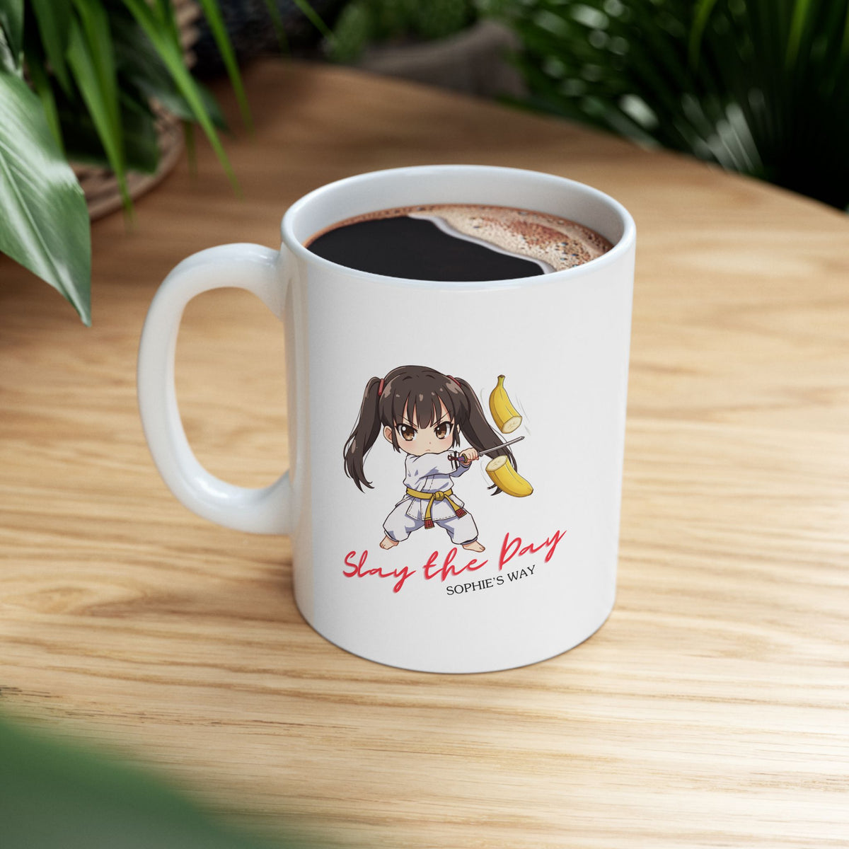 An 11oz mug with the image of a taekwondo girl slicing a banana with a sword with text that reads Slay the Day and Sophie's Way.