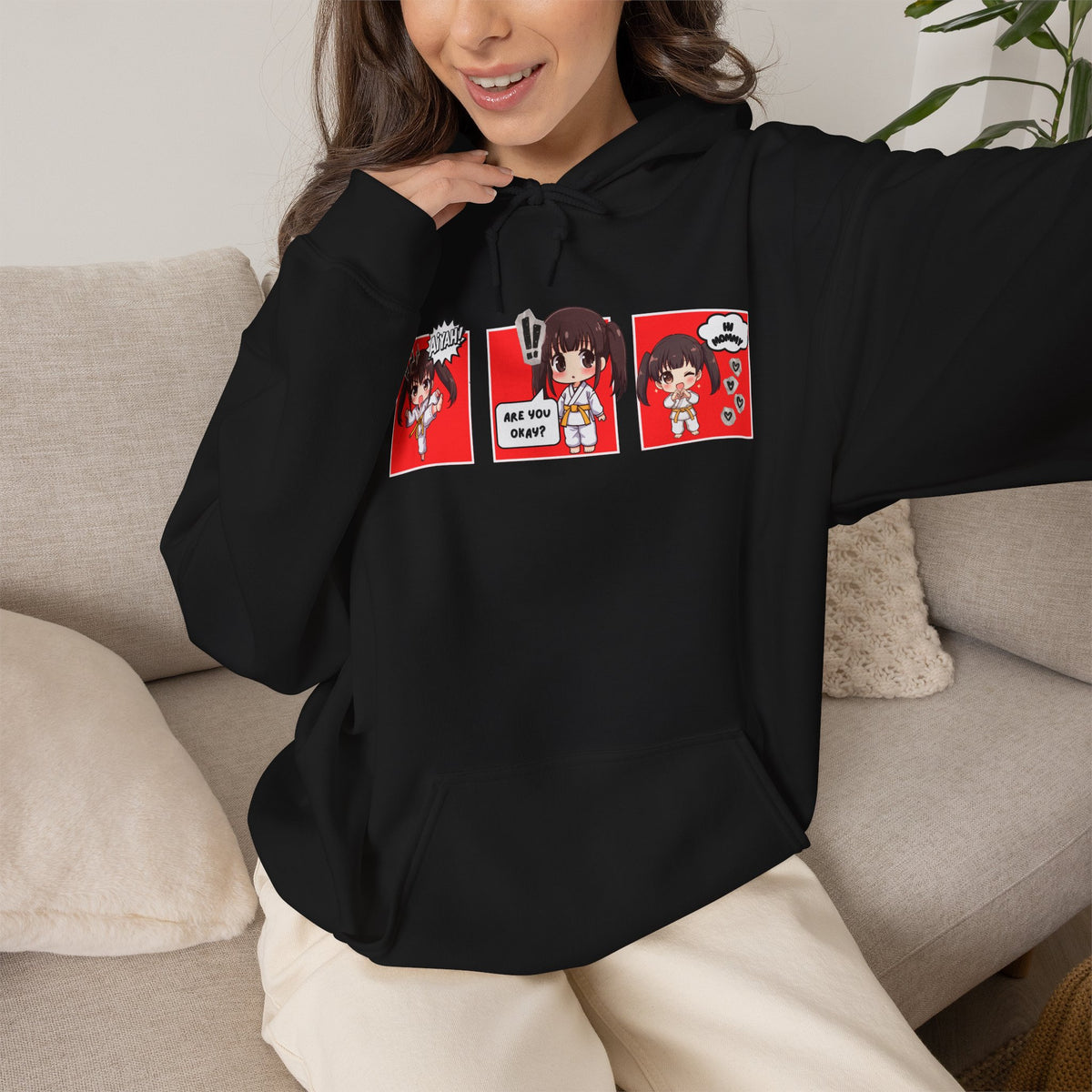 A black pullover hoodie with a red and multicolor anime-style graphic print on the chest of a taekwondo girl saying 'Aiyah!' then 'Are you okay?', and then 'Hi Mommy."