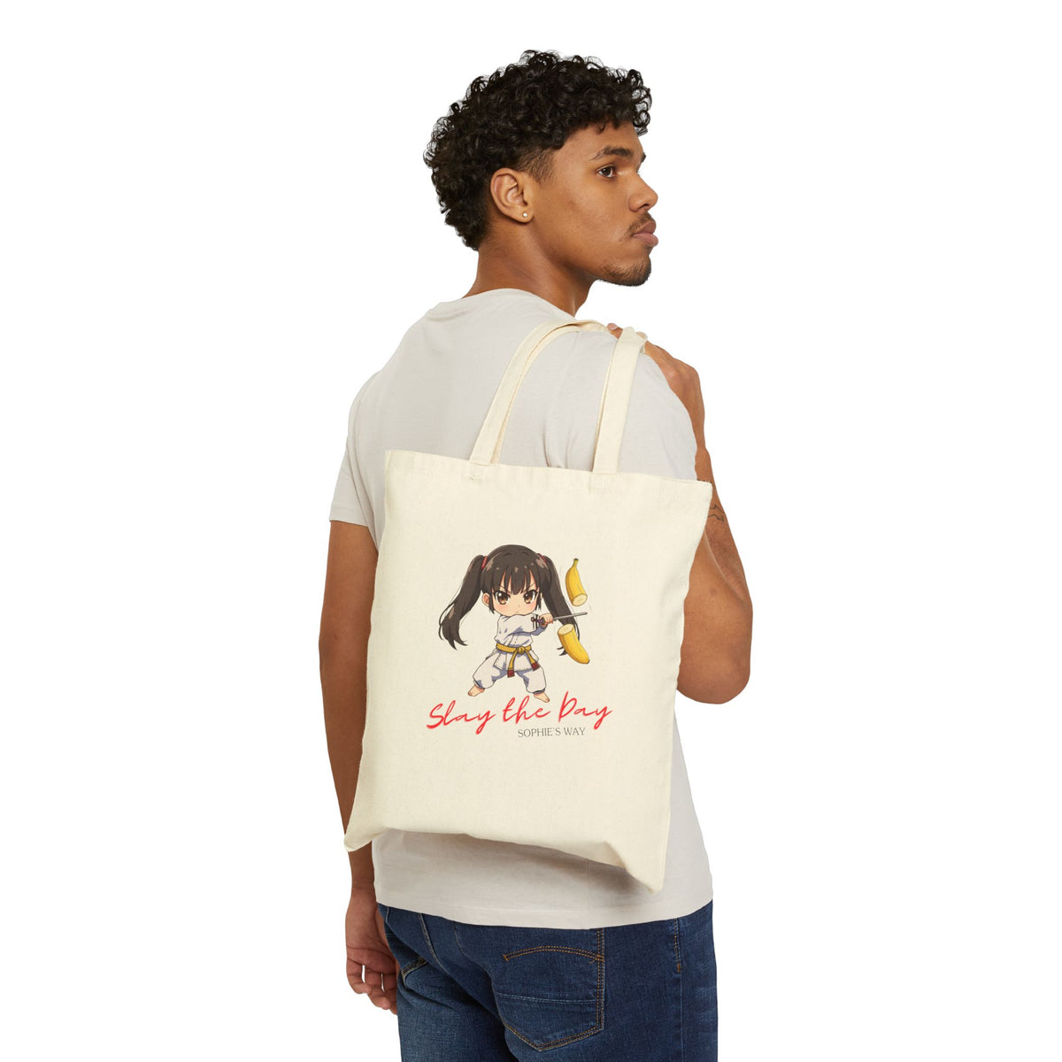 Slay the Day cotton canvas tote bag in natural, worn on back by man — chibi taekwondo girl slicing a banana with a sword — "Slay the Day, Sophie's Way"